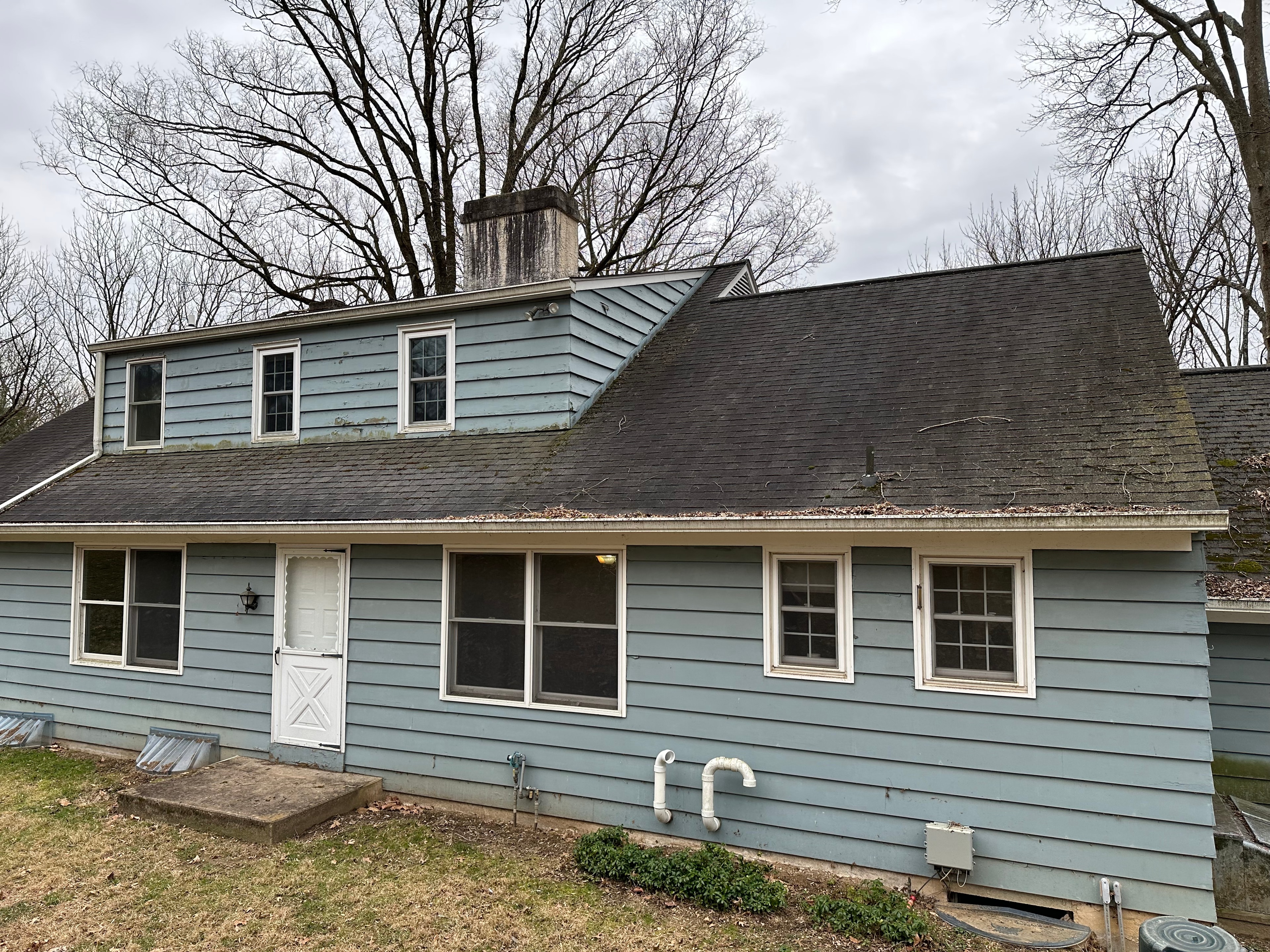 Rear of West Chester home showing original blue vinyl siding and dark aging shingles