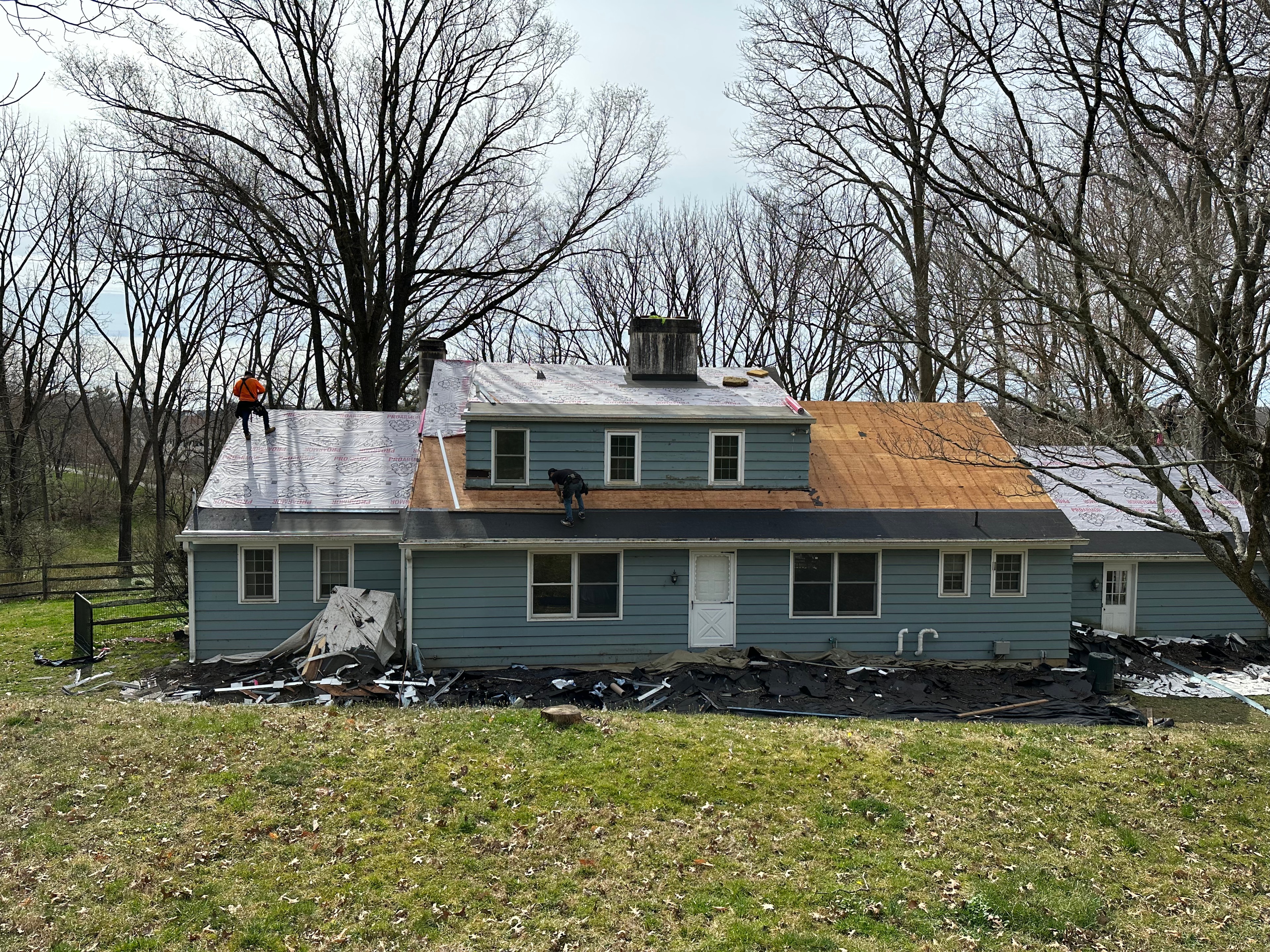 Crew performing roof tear-off on West Chester home with decking exposed and debris on ground